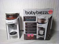 Photo of Baby Brezza Formula Pro Advanced formula dispenser unit next to its original box, showing front view and labeling.