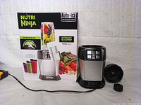 Ninja BL480D Nutri Ninja blender base with box, lid, and power cord, shown on white textured background