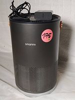 Front view of the black Smartmi air purifier showing brand logo and power cord with adapter placed on top.