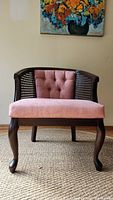 Front view of the tub chair with dark wood legs, pink tufted seat and back, and wicker side panels.