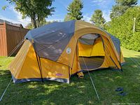 Front view of the tent showing yellow and gray fabric, door open with flaps, set up on grass with trees in background.