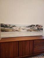 Full view of the wide horizontal canvas print depicting the landscape scene and its placement on a wooden cabinet.
