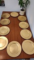 Top-down view of the 10 gold-colored charger plates arranged on a wooden table.