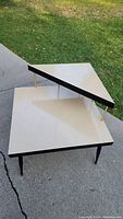 Side angle view of vintage two-tier corner table showing Formica surfaces, brass rods, and tapered legs with brass tips.