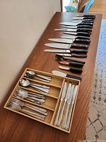 Photo of wooden cutlery tray with cutlery and additional knives arranged on table showing variety and condition.