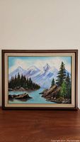 Frontal view of framed painting showing mountain scene with trees and lake