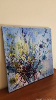 View of full abstract oil painting on canvas angled on wooden surface showing colorful impasto textures.