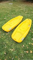 Two yellow Pelican Solo sit-on kayaks on grass showing top and bottom side views, highlighting the design and features including molded seating, footrests, and swim-up rear deck.