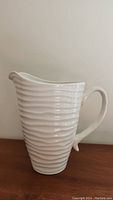 Full view of cream colored ceramic pitcher with ripple textured surface and spout.