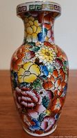 Full view of a brightly colored floral ceramic vase with varied large flower designs and a wide rim decorated with multicolor Greek key pattern.