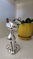Front angle of signed aluminum cat sculpture with closed eyes, sitting upright.