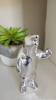 Front view of polished aluminum polar bear sculpture with raised right paw and smooth reflective surface.