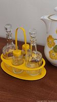 Photo showing four glass bottles (two with stoppers, two with yellow lids) sitting in a yellow metal tray.