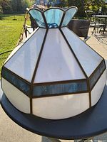 Angled view showing the pendant light's white and blue leaded glass panels with brass framing.