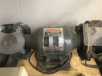 Front view of Durex 6 inch bench grinder showing overall body, dual grinding wheels and attached lamp.