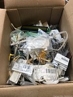 Box filled with assorted small electronic components including reels, small LCD displays, and parts in packaging.