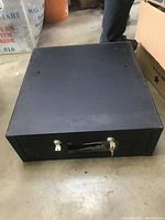 Large black rectangular cash box with keys on front slot, placed on floor surface