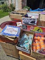 Boxes with assorted Halloween costume accessories and decorations outdoors on pavement with grass and building visible in background