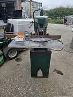 Front view of the green punch press machine on a metal base with scattered metal scraps on work surface, lamp mounted on top.