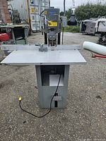 Front view of used punch press with metal work surface and foot pedal cord visible on pavement.