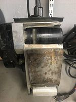 Close-up of belt sander showing sanding belt and metal housing with rust and wear.