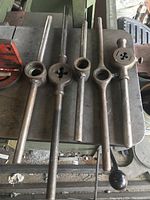 Five metal tool handles with threading die heads placed on a table; handles show wear and use, varying in die sizes and handle lengths.