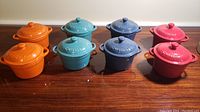 Eight mini casserole dishes with lids in four colors (orange, teal, blue, red) shown together on a wooden surface.