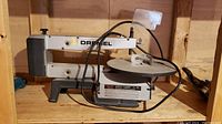 Full side view of the Dremel 16-inch scroll saw showing the main body, adjustable work table, and power cord.