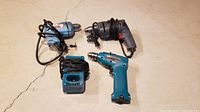 Lot overview showing all three drills including the two corded drills and the cordless drill with charger