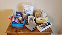 Omron blood pressure monitor and assorted first aid supplies on wooden surface including boxes, bottles, and baskets of medical items.