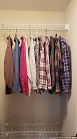 View of all 9 assorted men's button-up shirts hanging on a rack in a closet.