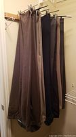 Five pairs of men's dress pants hanging showing different colors and cuff details with button side adjusters