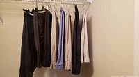 Eight pairs of men's shorts hanging on a rack, showing a variety of colors including black, dark gray, beige, light blue, navy, and white.