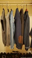 Five men's sweaters and jean jackets hanging on a rod; various textures and colors including browns, denim, and navy blue