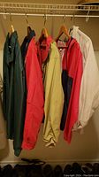 Full view of five windbreaker jackets hanging on a rack showing color and style variety.