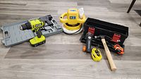 Full view of the lot showing the Ryobi cordless drill, orbital polisher, toolbox with assorted hand tools, and brad nailer on a wooden floor.