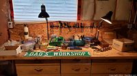 Photo of workshop bench with assorted screwdrivers mounted on pegboard wall behind and various small hardware items arranged on bench top including jars, boxes, and tools
