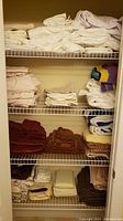 Closet shelf with multiple folded bed sheets and towels, showing white and light neutral linen sheets, and colorful towels on right side with some stacked brown towels below