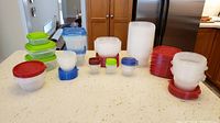 Overview of assorted plastic containers and lids arranged on countertop including red, green, blue lids, various sizes.