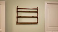 Front view of the solid wood wall hanging shelf mounted on a light green wall between two white door frames.