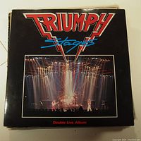 Front cover of the Triumph Stages double live album vinyl LP record showing band logo and live stage image.