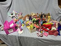 Overview photo showing the collection of Barbie dolls, doll clothes including handmade items, and accessories like a pink toy kitchen and bunny ear headbands
