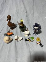 Photo showing nine assorted small bird figurines in various materials and colors on a fabric background.