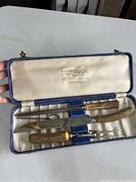 Open blue textured case showing three-piece carving set with bone handles and polished metal blades; satin lining with maker label.