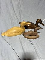 Three hand carved wood duck figurines in different wood finishes shown from the top view.
