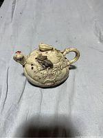 Carved small stone teapot with attached handle, short spout, and relief decorations of vines, leaves, and a butterfly on the side.