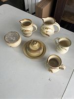 Photo of entire set of clay serving ware on white table showing all six pieces with wheat design and glass sugar bowl lid.
