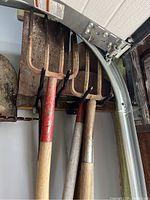 Shows shovels and rakes leaning against a wall with a garage door track beside them