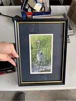 Framed heron painting showing front with natural bird scene and black frame with gold trim.