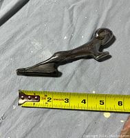 Photo of the metal Dodge Ram hood ornament measuring approximately 6 inches in length against a tape measure.